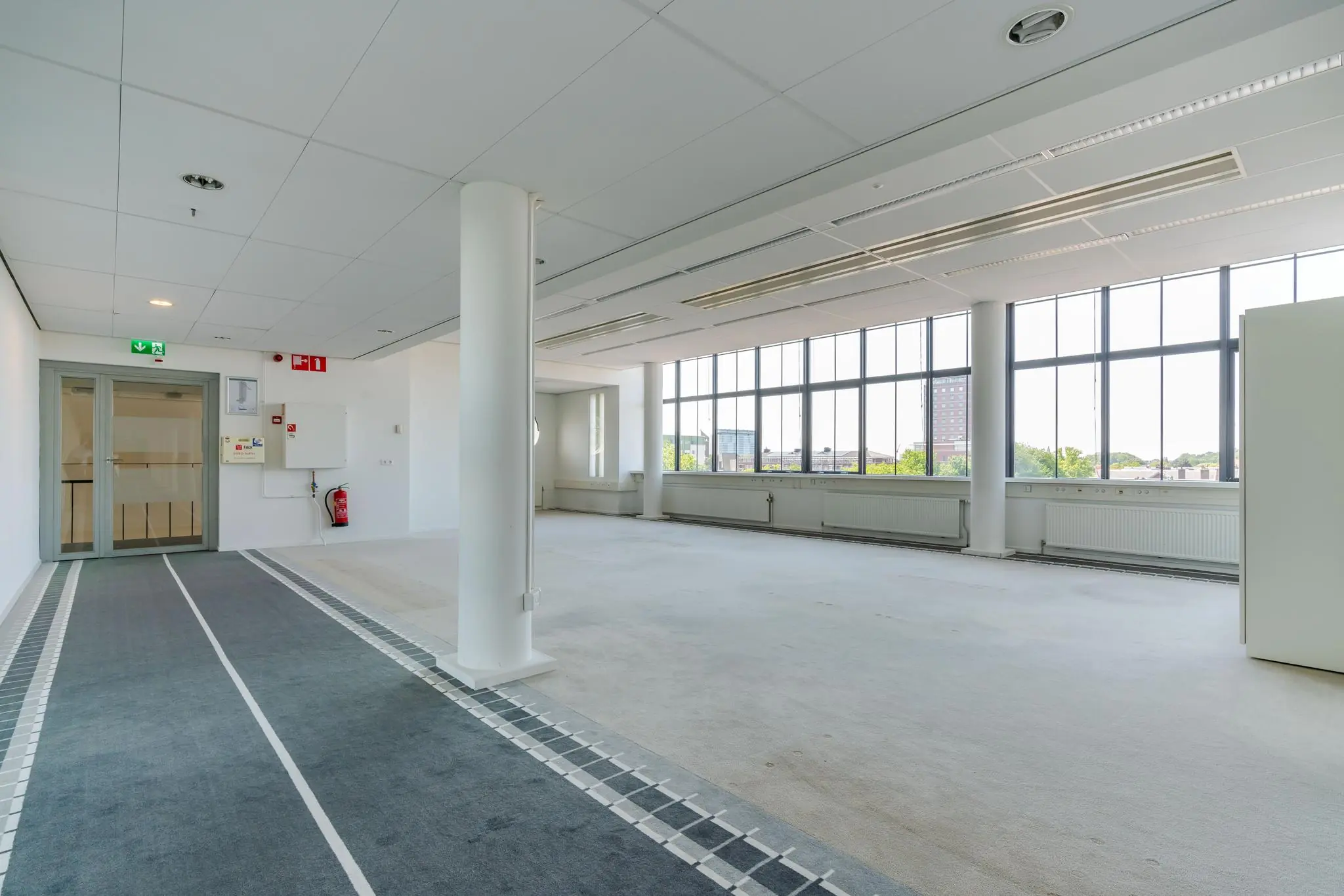 Lichte, lege kantoorruimte aan de Van Alkemadelaan met grote ramen en tapijtvloer.